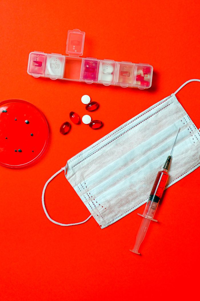 Flat lay of medical supplies including face mask, syringe, pills, and petri dish on a vibrant red background.