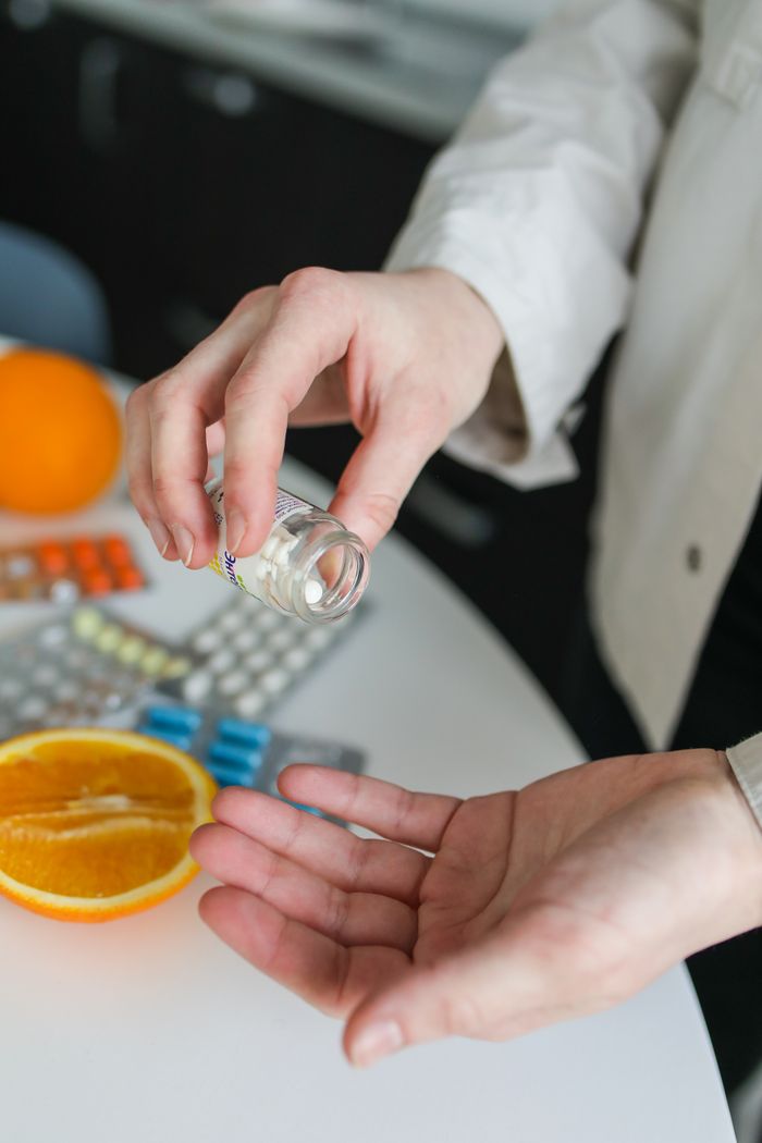 Close-up of person taking vitamins and pills beside fresh orange, emphasizing health and immunity.