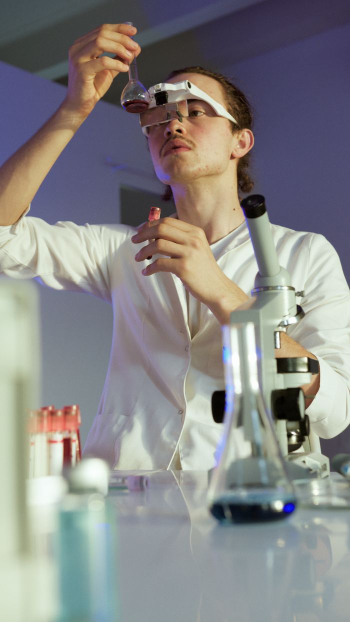 Young scientist in a laboratory carefully inspecting a sample, surrounded by lab equipment.